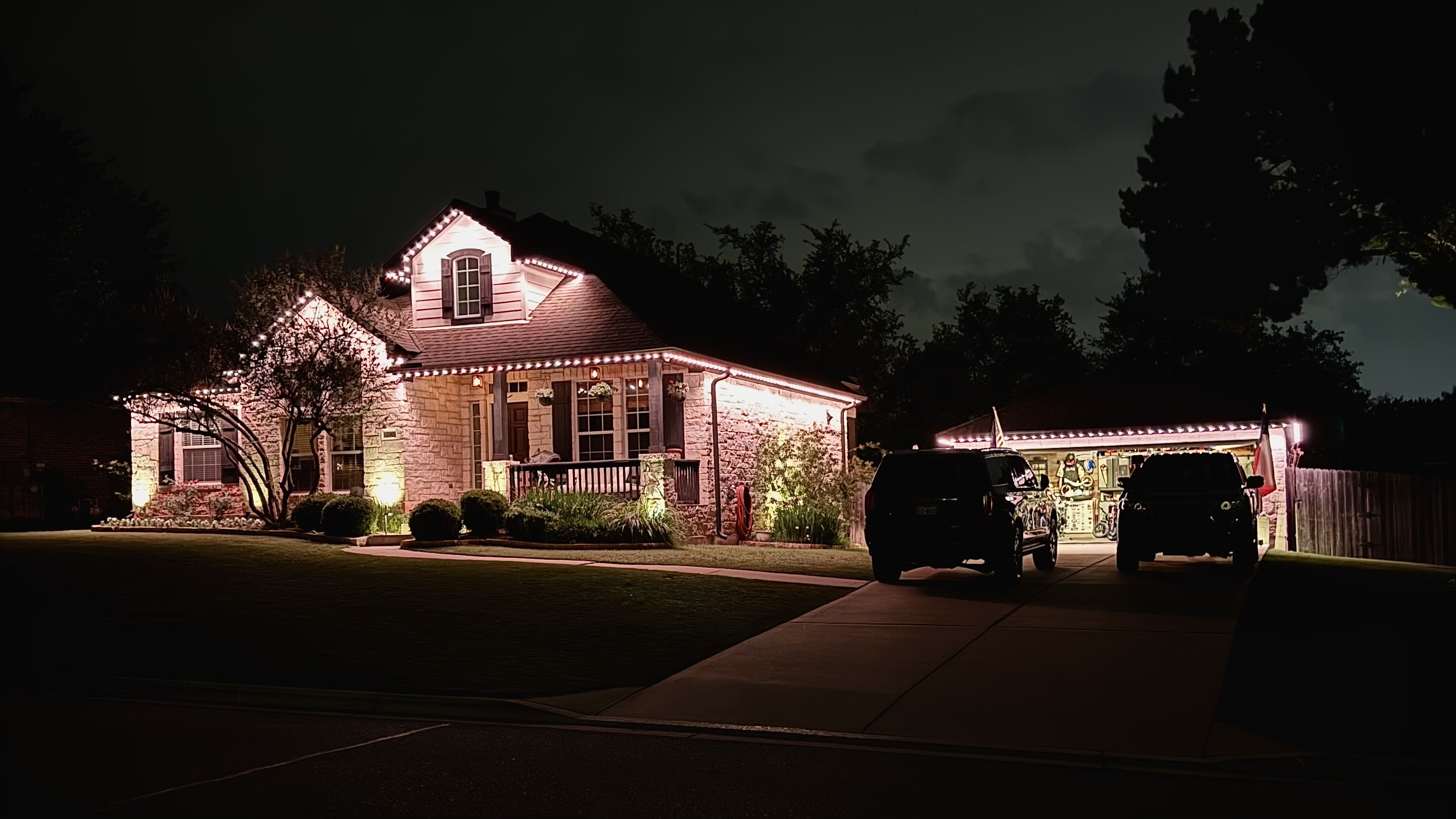 Craftsman home with security lighting and cars in driveway